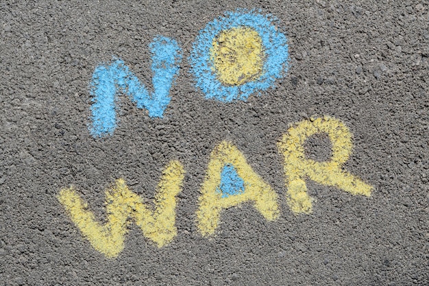 Слова "Нет войне", написанные синими и желтыми мелками на асфальте на открытом воздухе, вид сверху