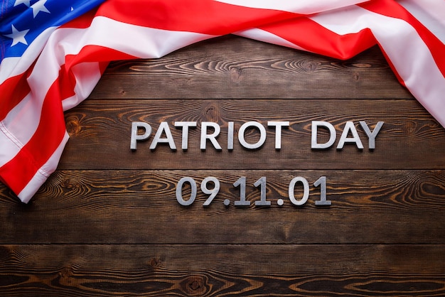 The words patriot day laid with silver metal letters on wooden board surface with crumpled usa flag