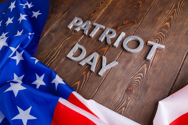 words patriot day laid with silver metal letters on wooden board with crumpled usa flag underneath