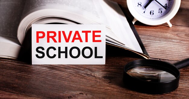 The words PRIVATE SCHOOL written on a white card near an open book, alarm clock and magnifying glass