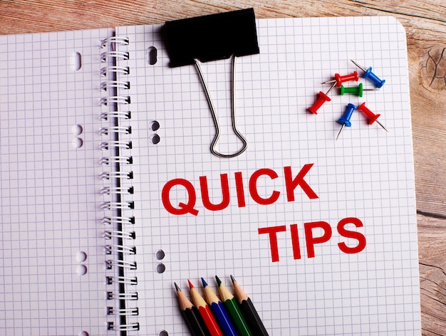 The words QUICK TIPS is written in a notebook near multi-colored pencils and buttons on a wooden surface