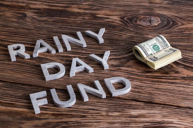 The words RAINY DAY FUND laid by metal letters near small pack of us dollars on wooden background