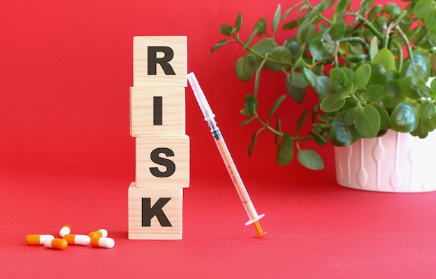 The words RISK is made of wooden cubes on a red table with medical drugs. Medical concept.