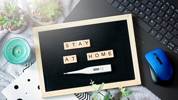 Words stay at home made of wooden blocks, concept of self quarantine at home as preventative measure against virus outbreak. Flat lay, laptop, note books, staying at home during emergency