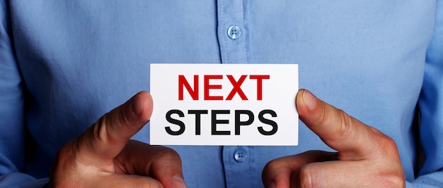 The words NEXT STEPS is written on a white business card in a man's hands. Business concept