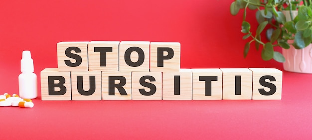 STOP BURSITIS라는 단어는 의료용 약물과 함께 빨간색 표면에 나무 큐브로 만들어져 있습니다.