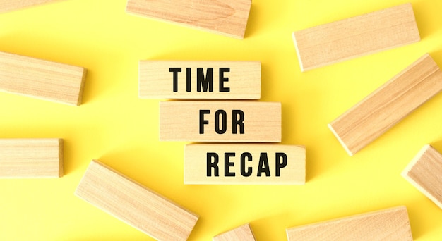 The words time for recap are written on scattered wooden blocks on a yellow background