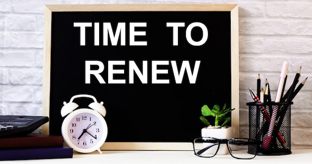 The words TIME TO RENEW is written on the chalkboard next to the white alarm clock, glasses, potted plant, and pencils in a stand..