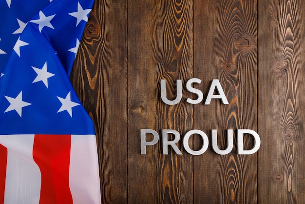 미국 국기와 함께 갈색 나무 표면에 은색 금속 글자로 놓인 USA 자랑스러운 단어