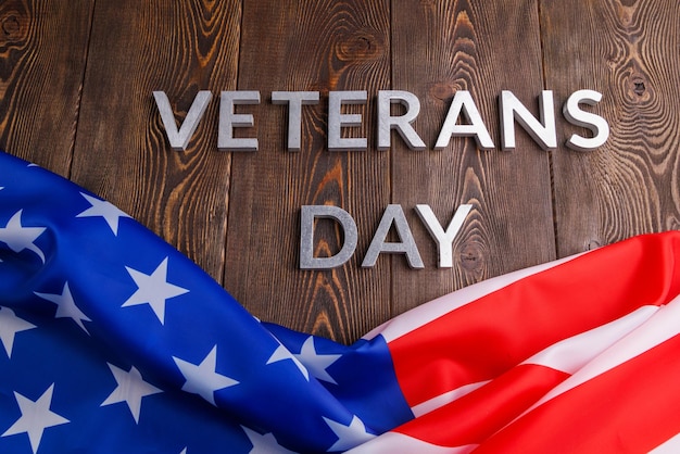 Слова день ветеранов выложены серебряными металлическими буквами на поверхности деревянной доски со скомканным флагом сша