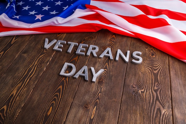 The words veterans day laid with silver metal letters on wooden board surface with crumpled usa flag