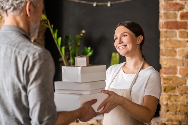 Work, colleagues. Happy woman in apron and man standing with back to camera passing packing boxes to each other at bakery