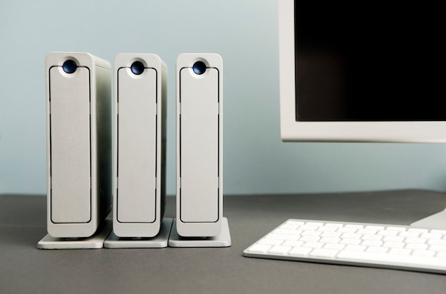 work desk recording computer base station with three silver hard drives stack partial view of silver computer monitor and white and silver keyboard black background