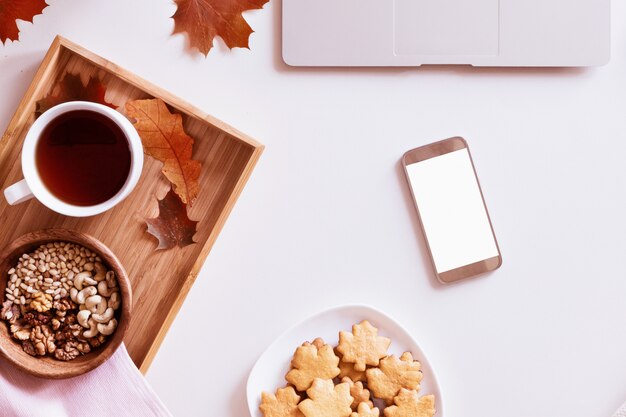 Work desk with laptop, coffee cup, cookies, smartphone and autumnal leaves. Top view