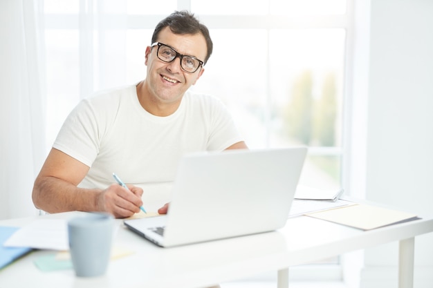 Work at ease latin man in white t shirt and eyeglasses smiling at camera while