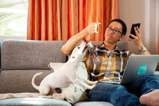 Работа из дома. Азиатский человек работает и проверяет документы с ноутбуком и играет со своей собакой в офисе.
