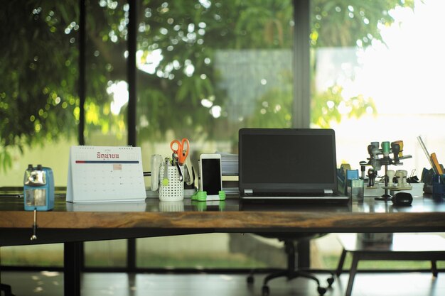 Photo work from home concept closeup laptop on the wooden table surrounded by the office stationaries