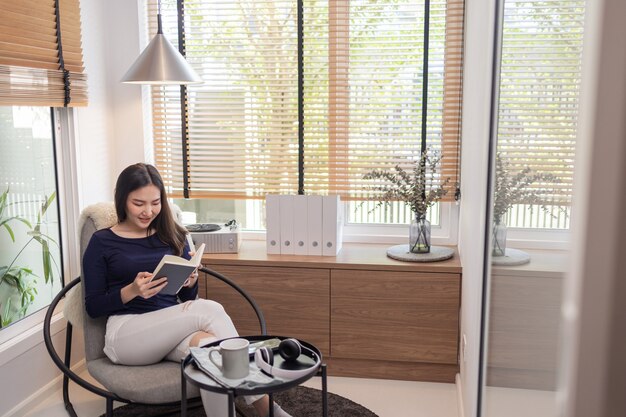 Work from home concept a pretty woman sitting on a modern chair in a well- decorated minimal room reading a famous book.