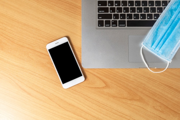 Work from home concept. Top view laptop, smartphone, and face mask on wood table .