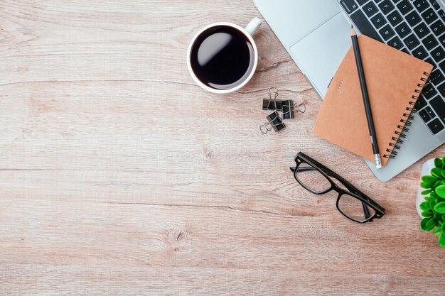 Work from home desk office with laptop blank notepad coffee cup\
and pen on wood table flat lay top view copy spce