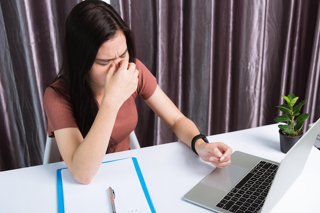 집에서 일하고, 피곤하거나 긴장된 아시아 비즈니스 젊은 미모의 여성은 사무실에서 오랫동안 노트북 컴퓨터 화면을 본 후 눈을 감고 피곤함을 느끼며 책상 작업 공간에 앉아 있습니다.