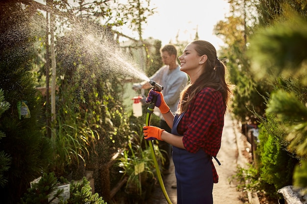 Work in the garden. Girl gardener sprays water and a guy sprays fertilizer on plants in the beautiful nursery-garden on a sunny day. .