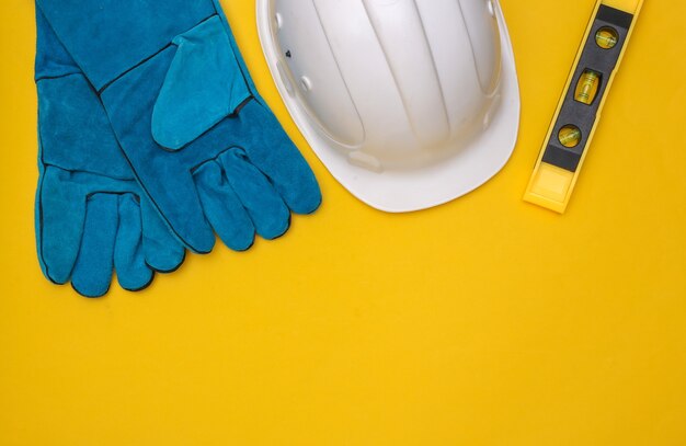 Work gloves, level and construction safety helmet on yellow background. Copy space. Top view