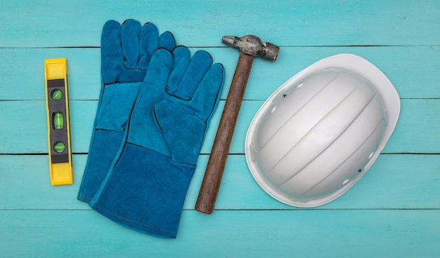 Work gloves, level, hammer and construction safety helmet on blue wooden background. Top view