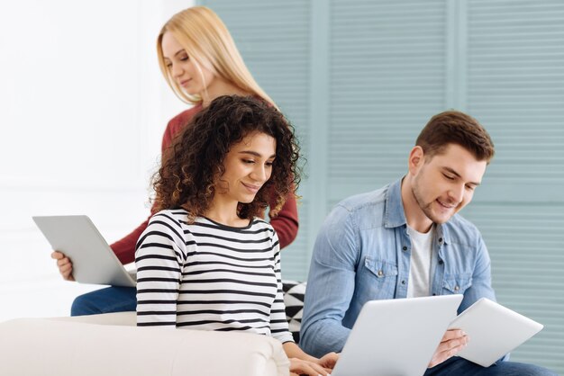 Work in group. Attractive brunette smiling while looking at screen of computer and spending time with pleasure