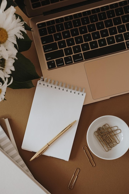 Work at home concept Flatlay of aesthetic minimalist workspace Notebook sheet with copy space stationery and laptop computer on tan beige background Flat lay top view