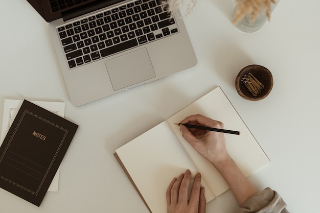 Work at home concept. Flatlay of aesthetic minimalist workspace. Woman write notes in notebook