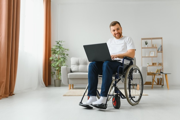 Work at home Paralyzed male person holding laptop on knees and keeping smile on face while looking at screen