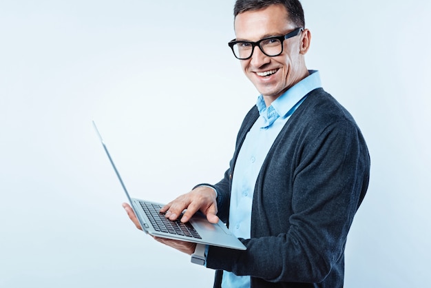 Work is calling. Side view on a successful entrepreneur turning his head into the camera and beaming while working on a project with his computer in hands.