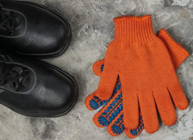 Work leather shoes and gloves on gray concrete background. Safety gear. Top view