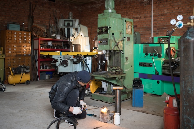 Work man is a welder in mask, metal product at home garage, with flame burning gas welding