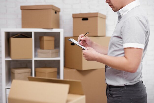 Work, people and business concept - close up of male hands writing something in clipboard in warehouse