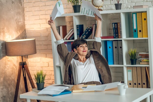 직장에서. 사무실에 있는 테이블에 앉아서 일하는 단발 중년 여성