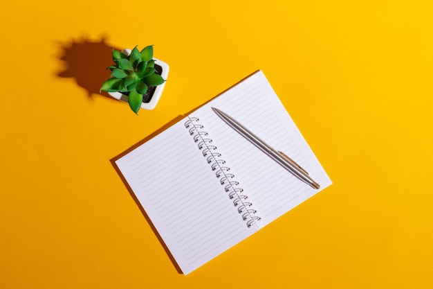 Work table with open notebook and flower on bright yellow background