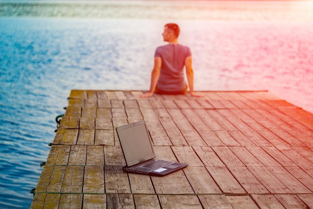 Work and travel Young man using laptop computer sitting on wooden fishing pier with beautiful sea view