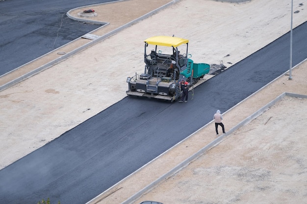 駐車場用の建設現場にアスファルトを敷設する労働者とアスファルト舗装機械、トップビュー