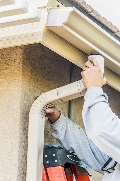 Photo worker attaching aluminum rain gutter and down spout to fascia of house