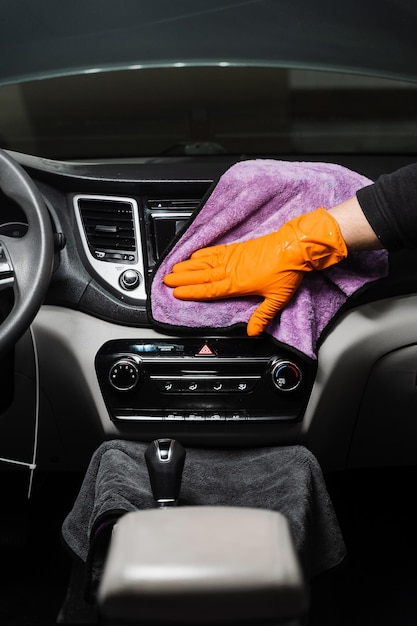 Worker in an auto detailing service is using microfiber cloth to manually dry the interior of car specifically the dashboard area