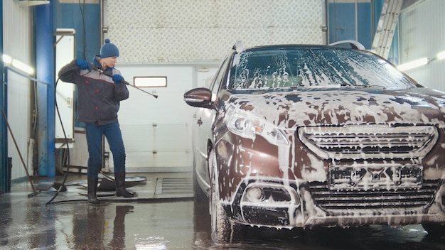 自動車サービスの労働者は、水ホースで泡の中で車を洗っています