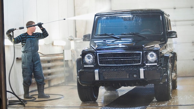 Worker in auto service is washing a luxury car in the suds by water hoses telephoto