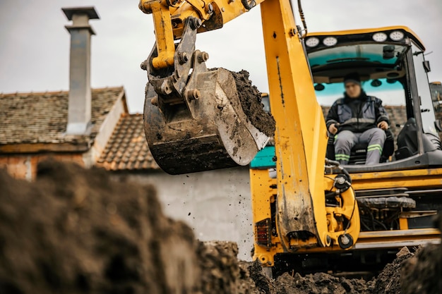 A worker in a backhoe is digging pit on a reconstruction area