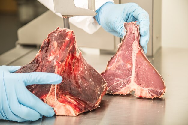 고기 가게에서 밴드 톱의 작업자가 고기를 자른다. 시장에서 T-Bone 스테이크를 자르거나 자르십시오.