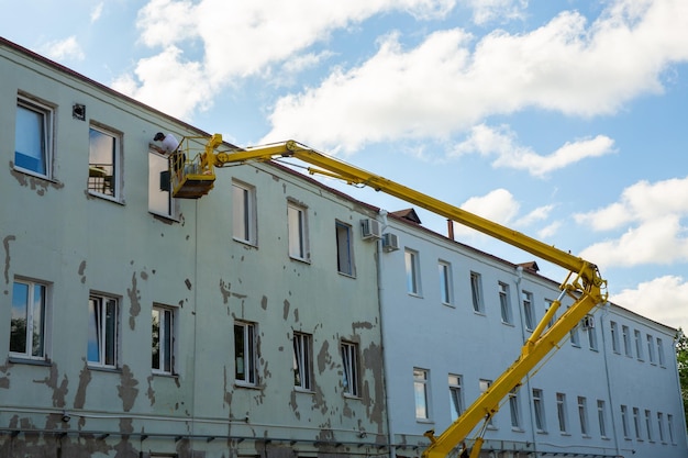 Photo worker in the basket of a car lift are repairing the facade of administrative building