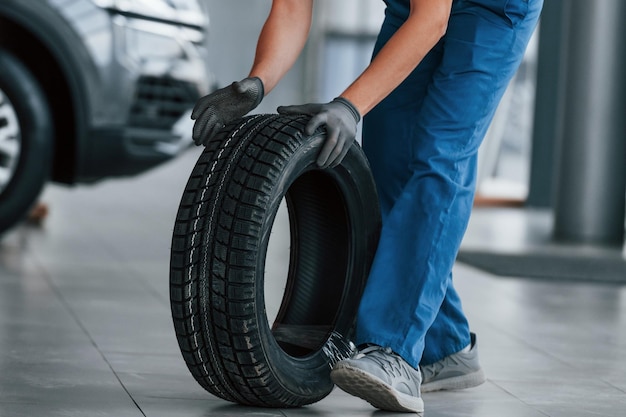 Worker in black and blue uniform holding car wheel and have job indoors