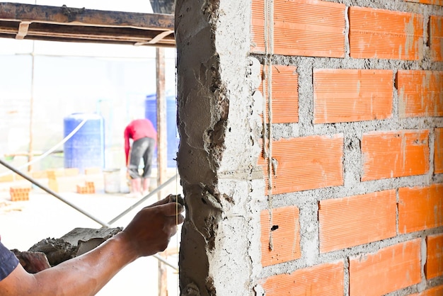 Foto muratore operaio che scava malta mista su mattone per installare il blocco di mattoni sul cantiere