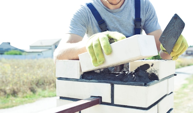 Il lavoratore costruisce un palo di recinzione dai mattoni